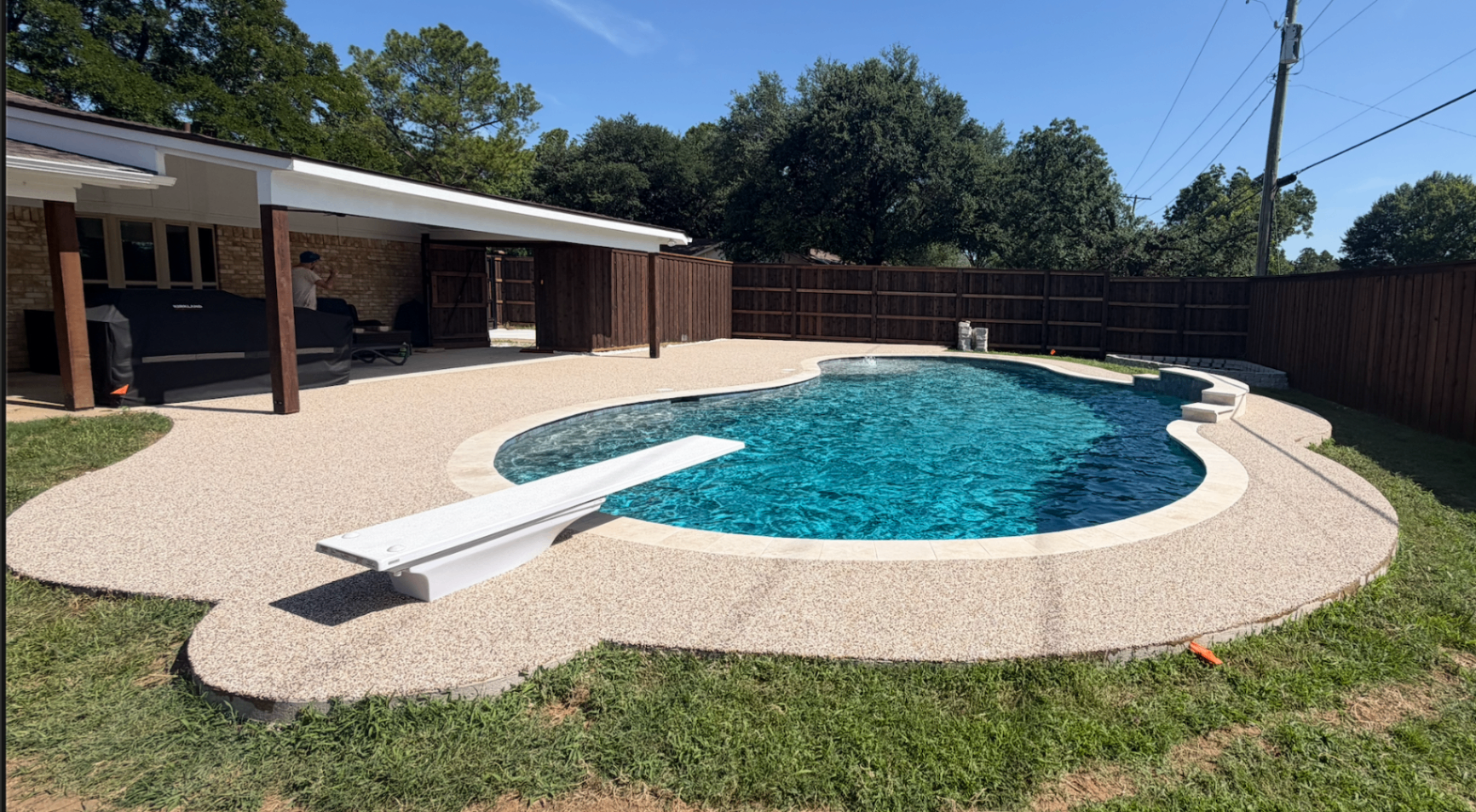 Finished rubber surfacing pool deck with diving board at a Lubbock backyard project